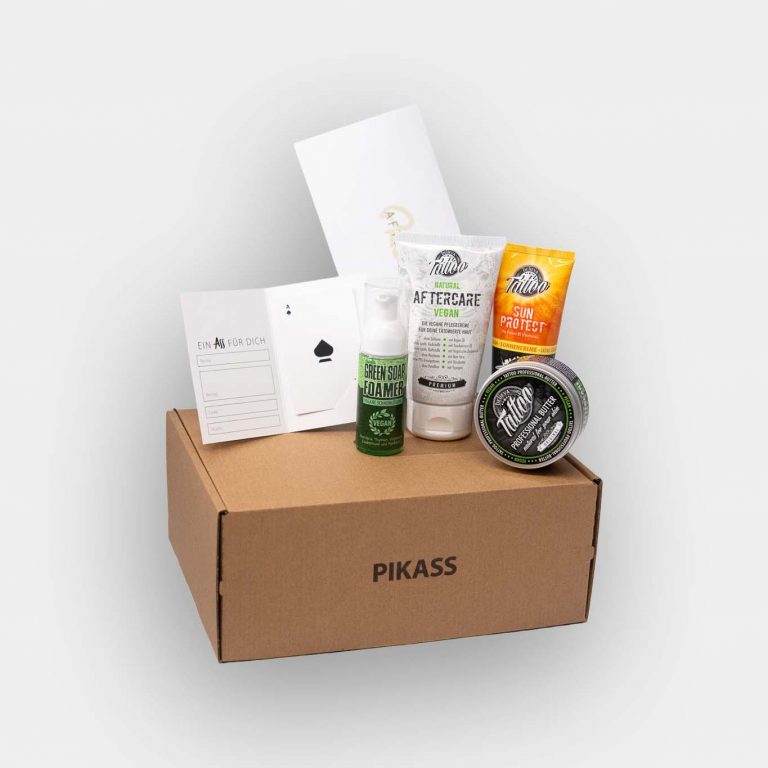 PIKASS Tattoo Geschenkbox M mit Tattoo-Gutschein, Aftercare Guide, Green Soap, Sun Protect, Tattoo Butter und Tattoo Pflegecreme auf grauem Hintergrund